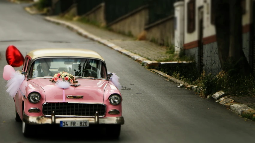 a pink car with hearts attached to it and pink balloons