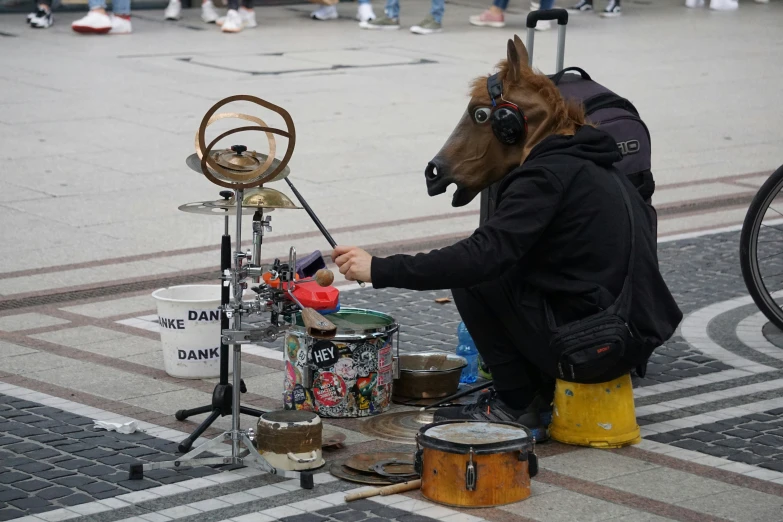 man in horse mask and leather hood plays with drum set