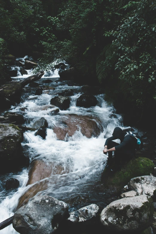 person sitting on rock next to rushing river