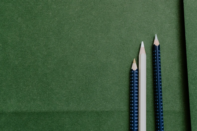 two blue and white pencils sitting side by side on green paper