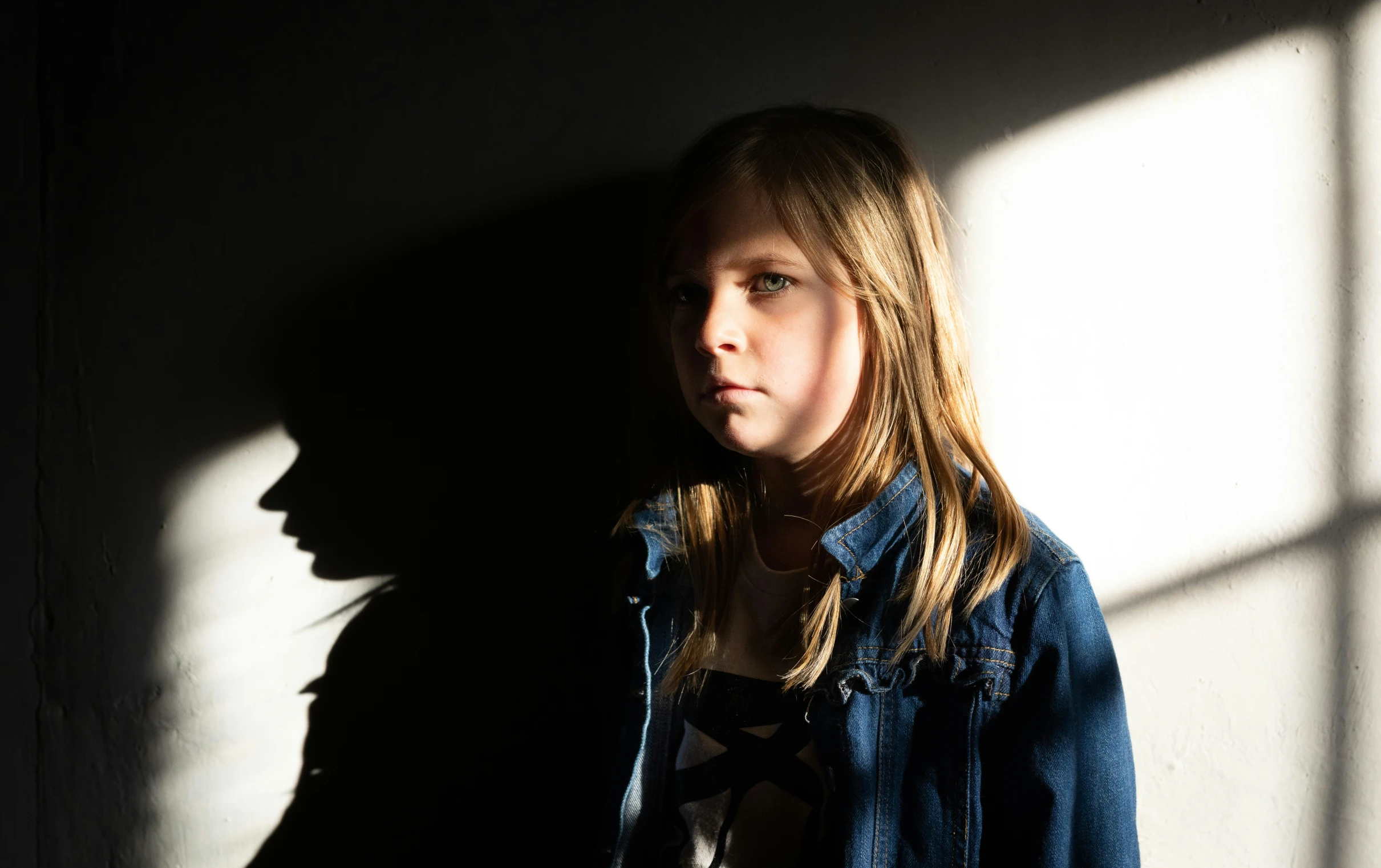 a woman in a denim jacket is standing against the wall