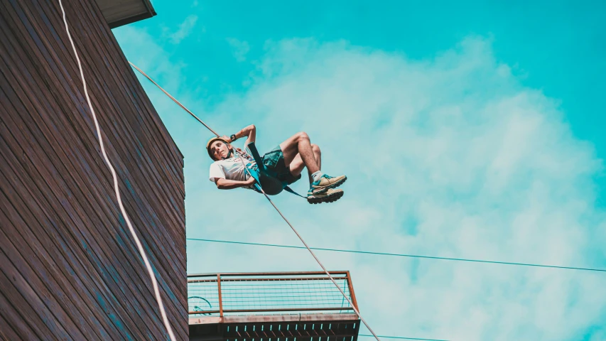 a man hanging from the side of a high rise building while holding onto ropes