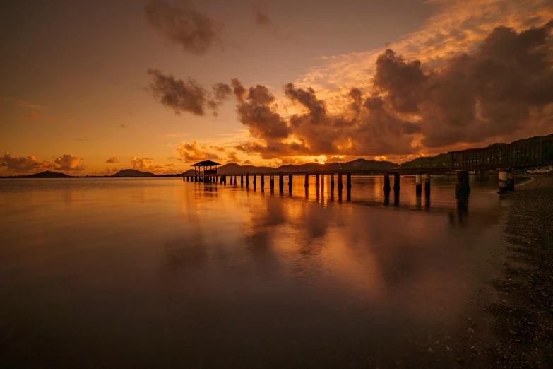 a jetty stands out on the water with clouds over it at sunset