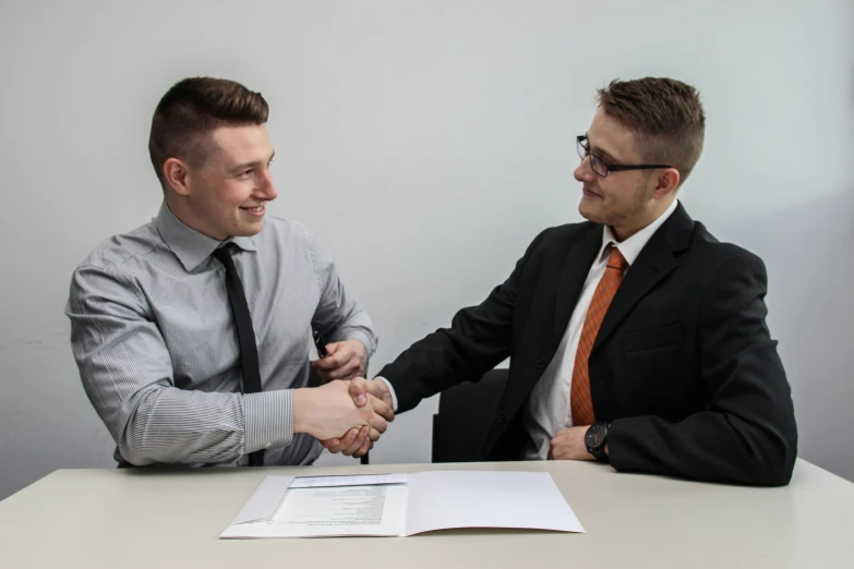 two men are shaking hands at a desk