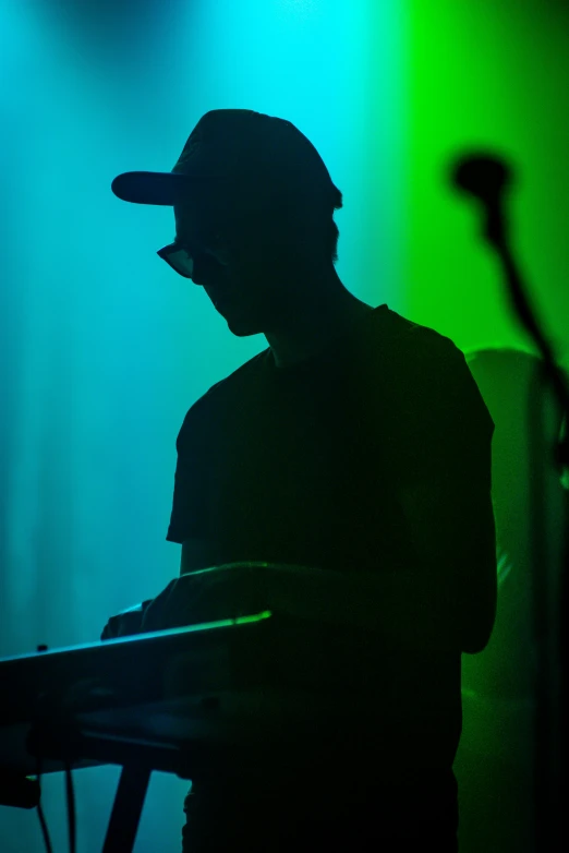a man stands at a keyboard in front of green and blue lights