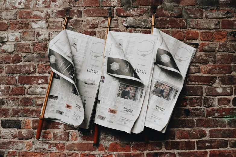 four newspapers hanging on a brick wall