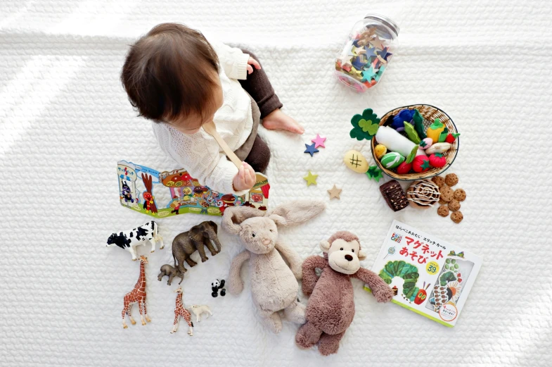 an infant girl standing next to many toy animals