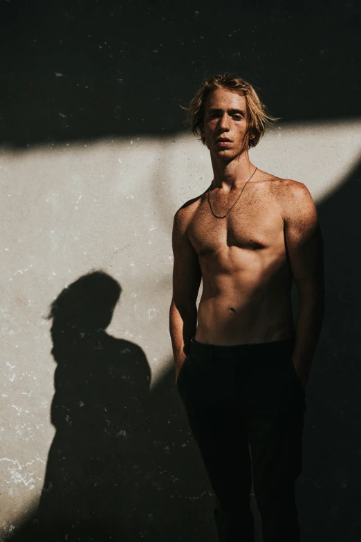 man with long hair is standing in front of a white wall and has  on