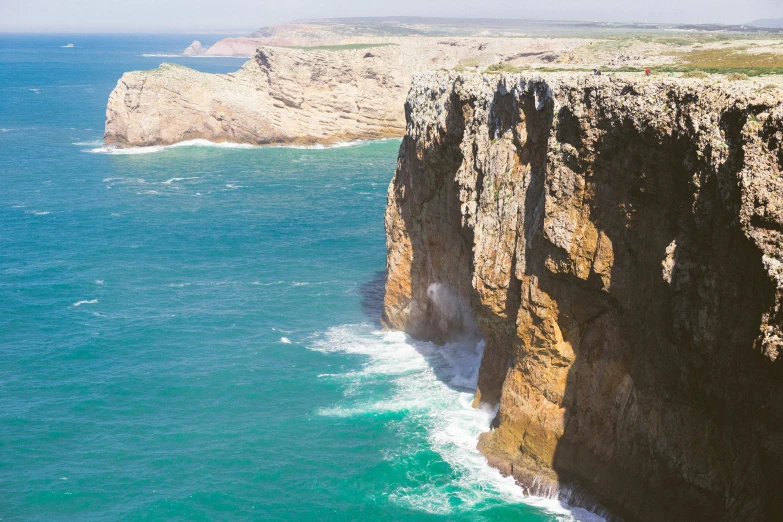 some cliffs and water with a white boat in the ocean