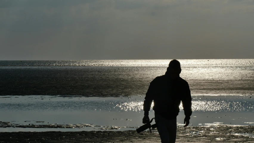 man in the distance, walking along a beach, with his dog in front of the water