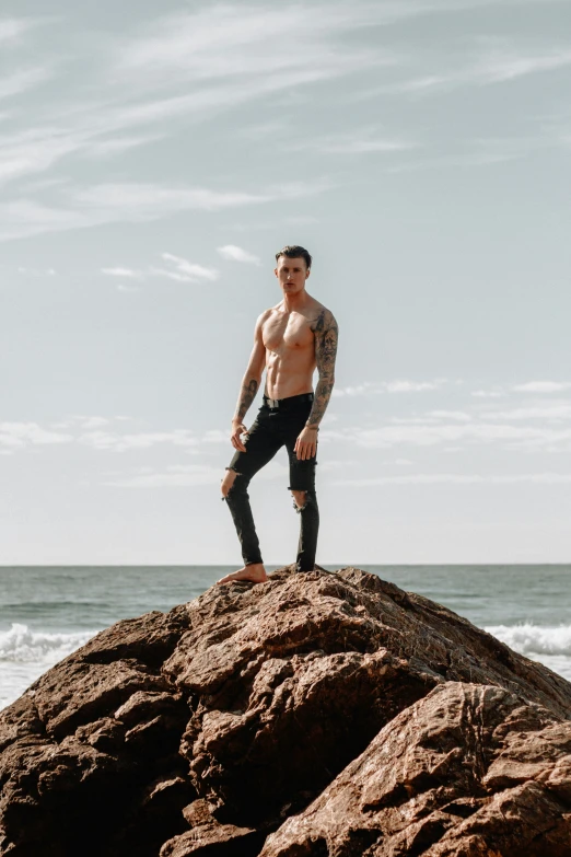 shirtless man standing on rocks overlooking the ocean