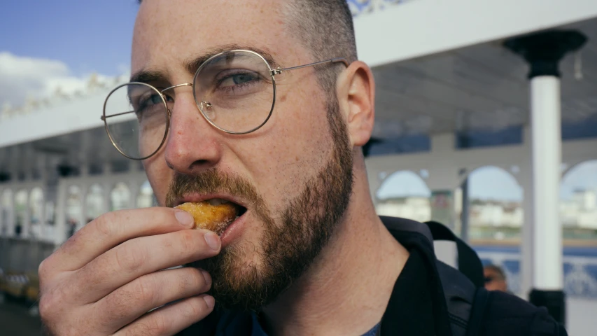 man with round glasses eating a donut in a station