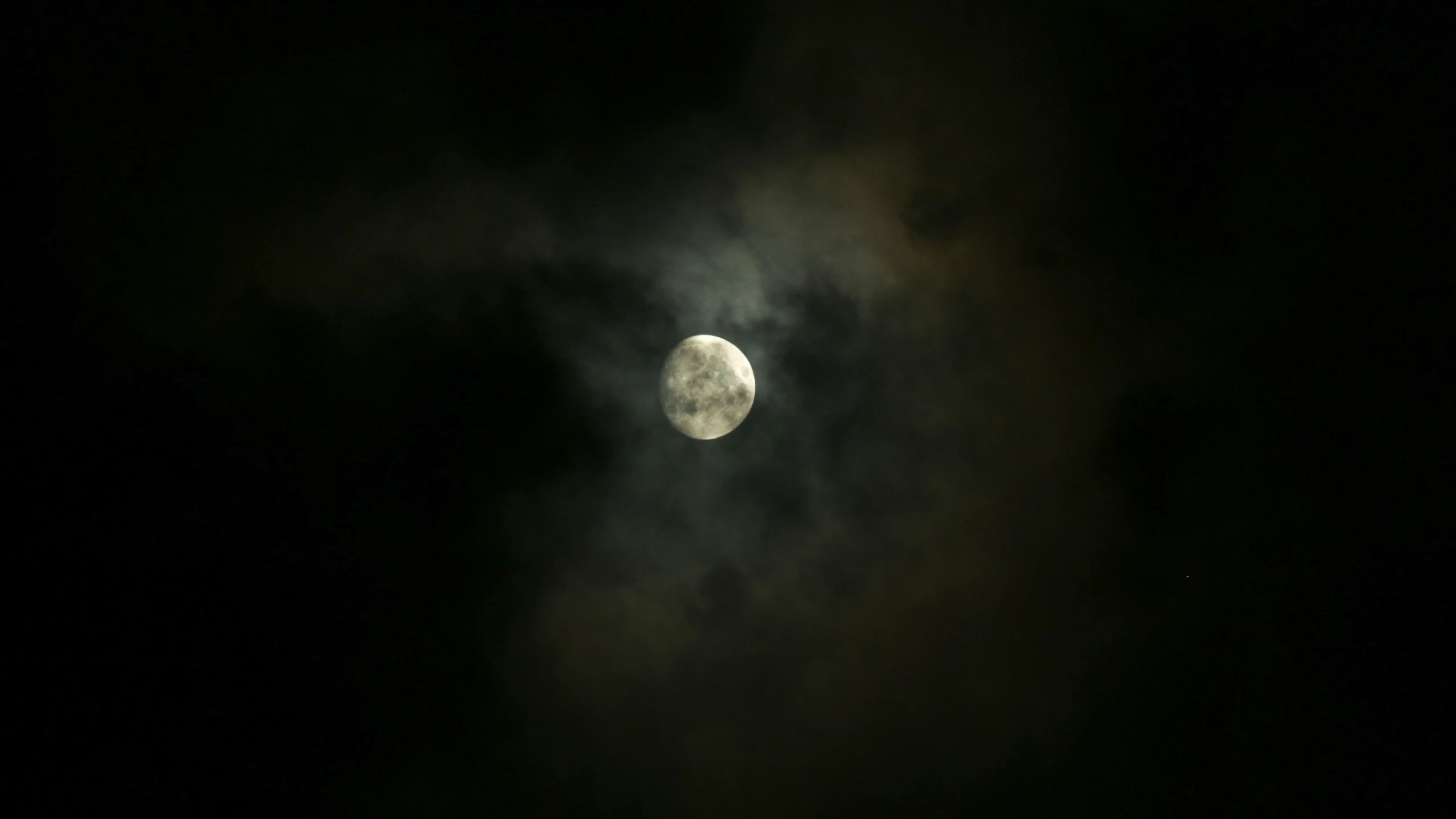 the moon shining through the dark clouds