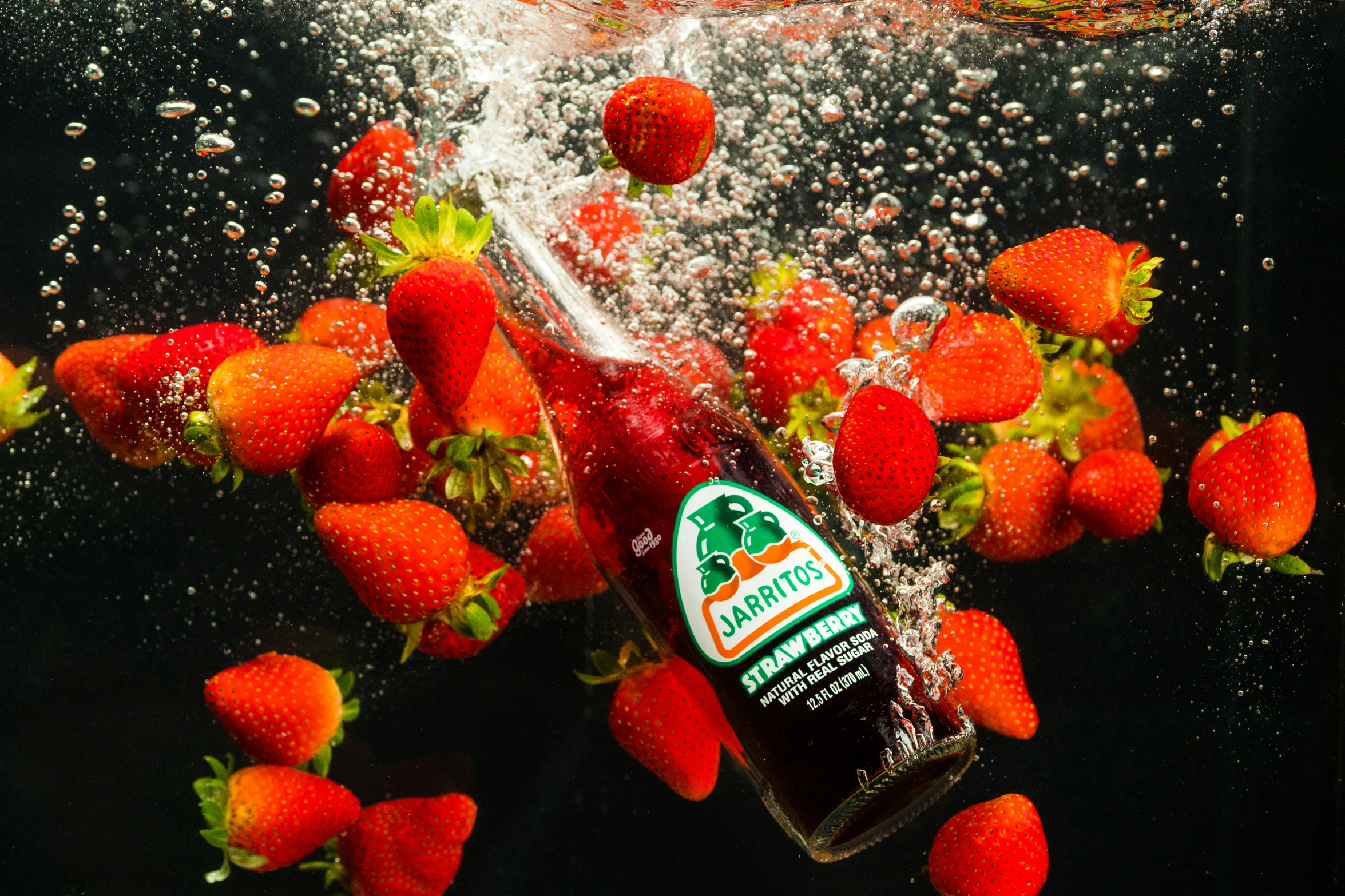 a bottle with water splashing down over strawberries