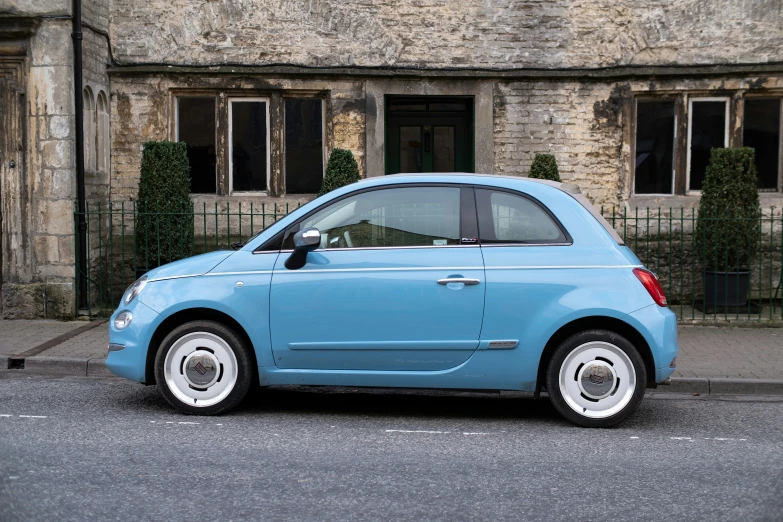 small, blue car parked on asphalt next to building