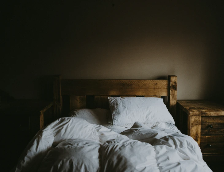 an unmade bed sitting next to a night stand