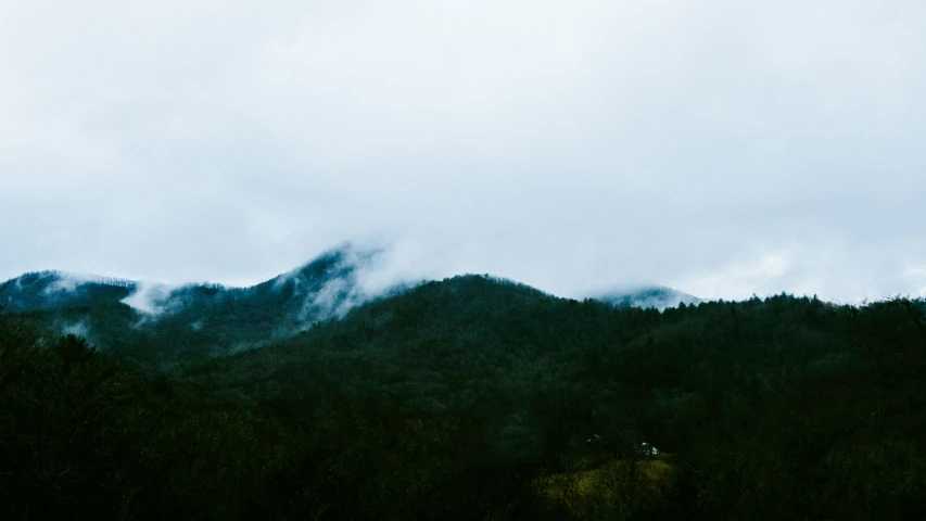 a group of trees and mountains with the sky covered in clouds