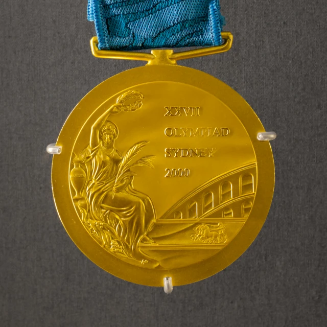 an olympic medal with an award ribbon hanging on a grey wall