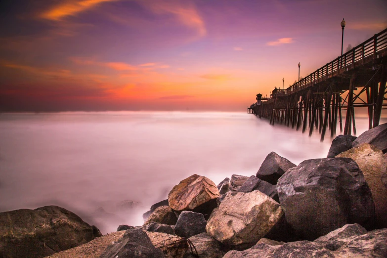 the water and rocks near the pier is reflecting the sky