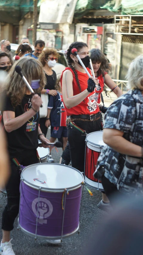 women dressed in red drumming with drums on a city street