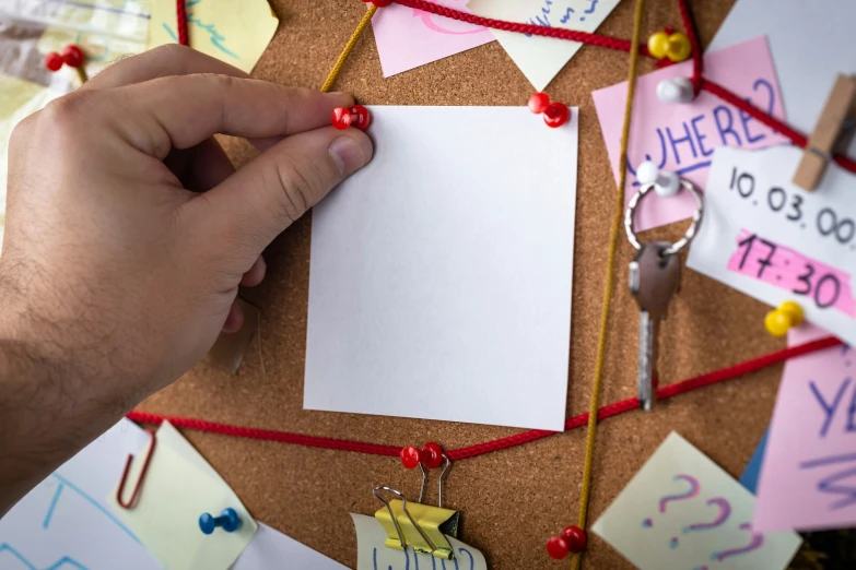 a person holds a piece of paper in front of a cork board that has several notes on it