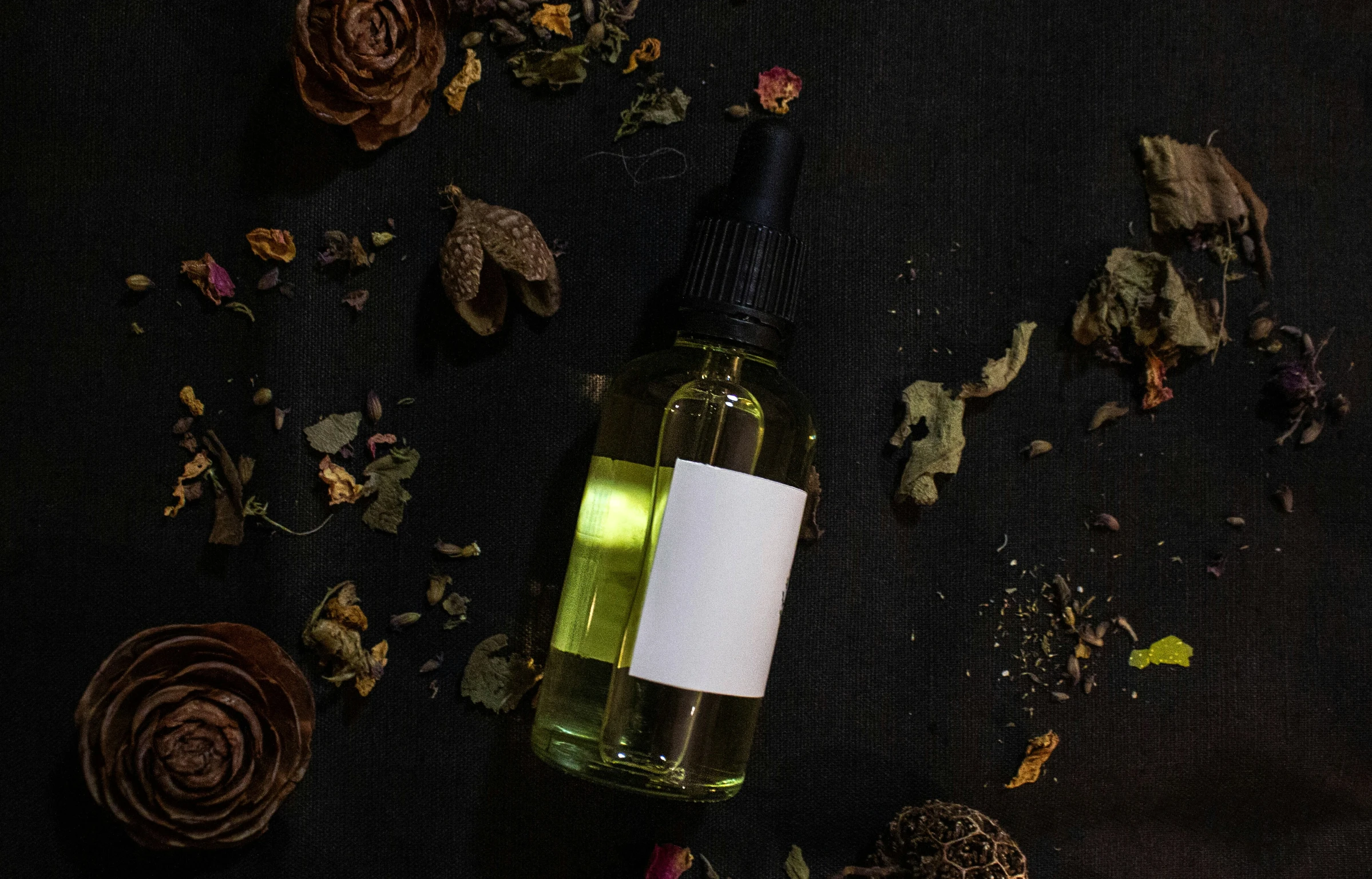 a bottle filled with green liquid next to an dried flower