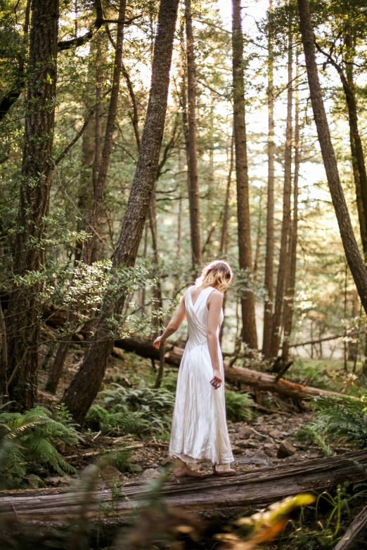 a woman stands in a wooded area on a log