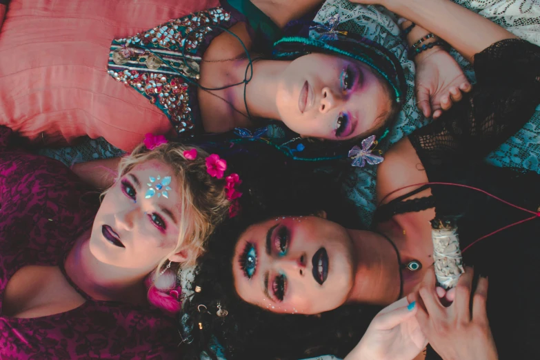 three girls lay down on the ground wearing makeup