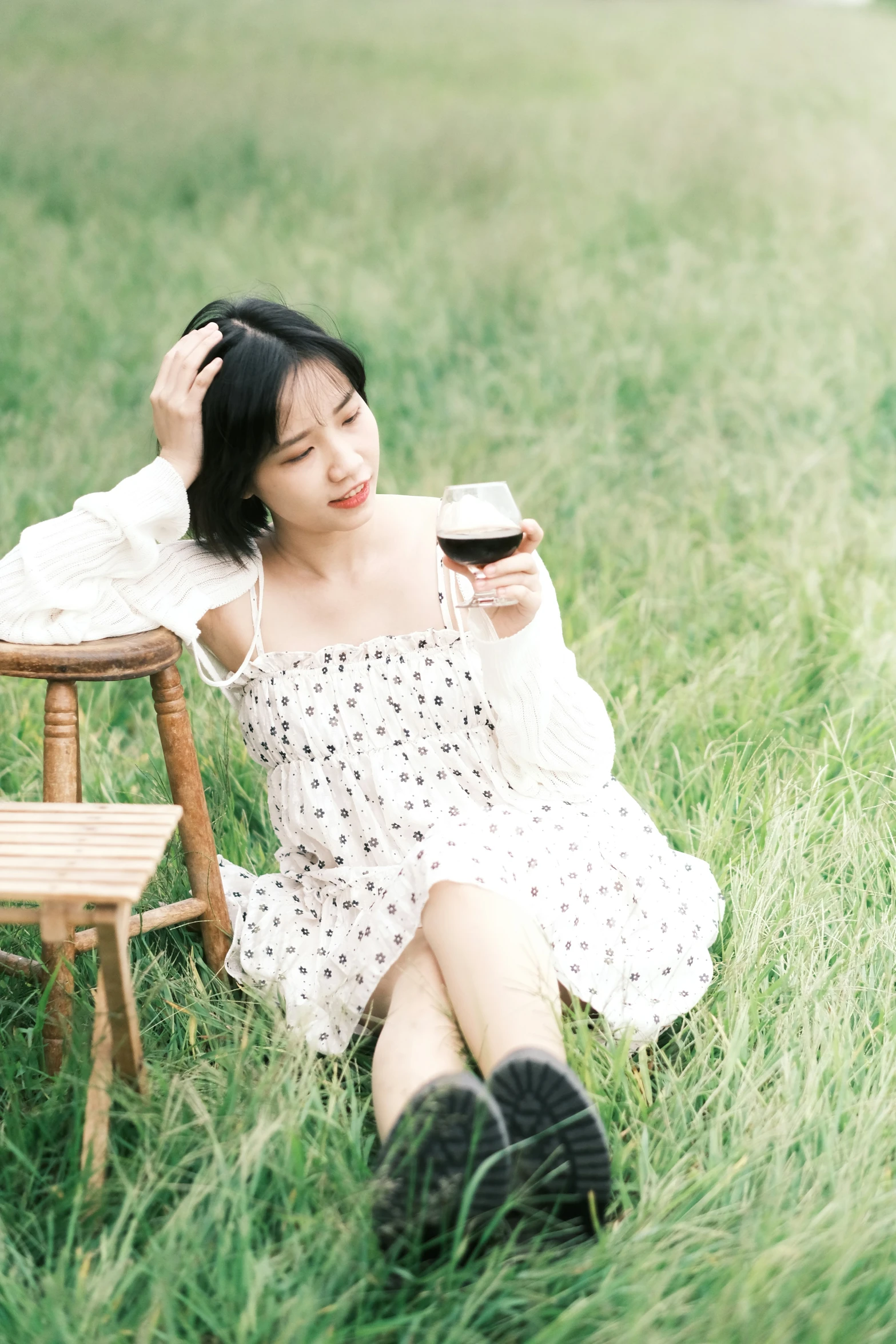 a pretty young lady sitting in a field with a cup of coffee