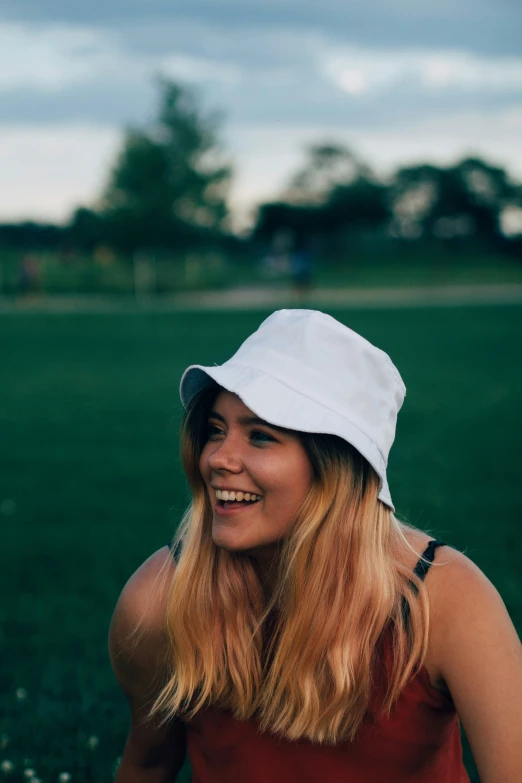 a woman in a white hat smiles on a grassy field