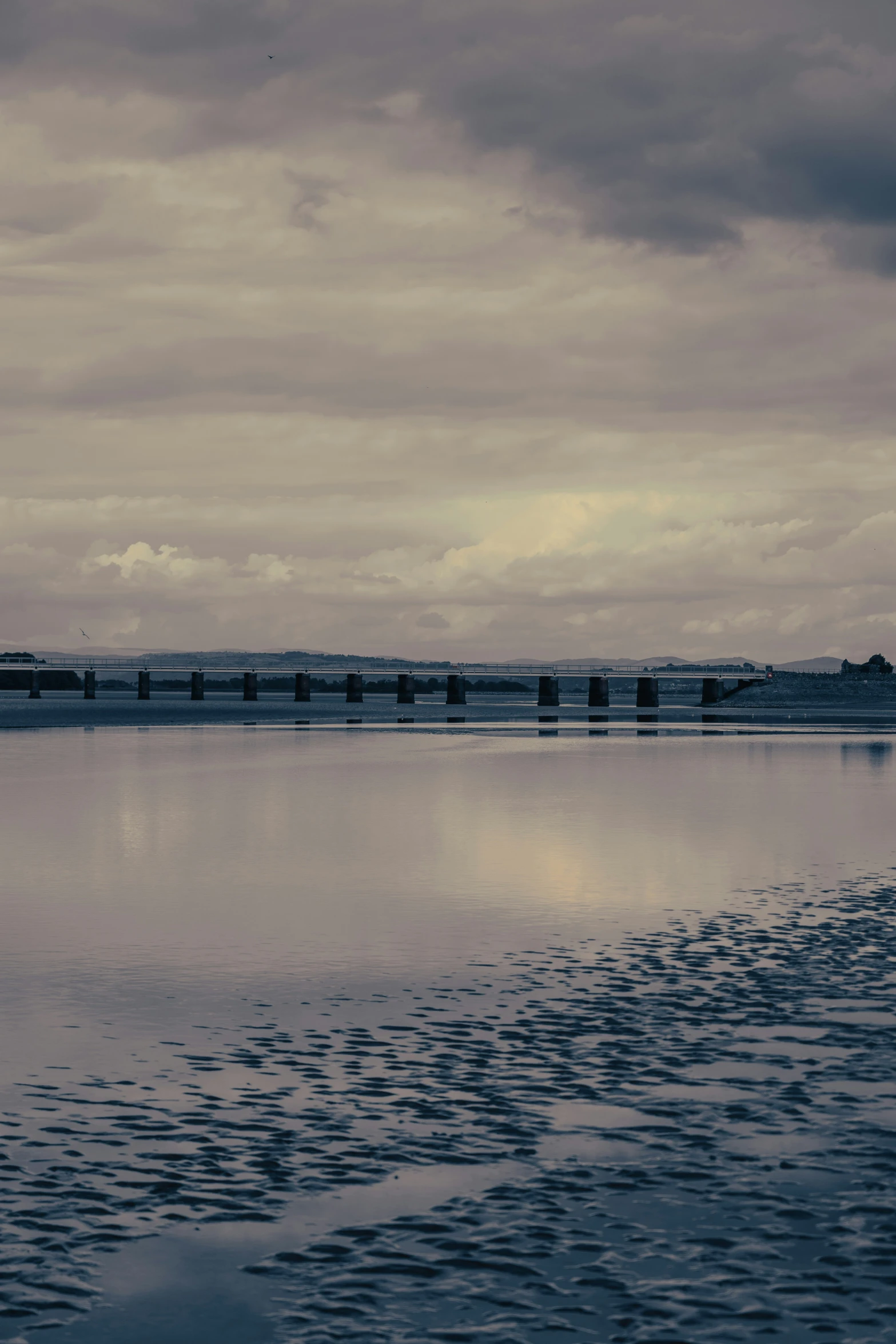 a cloudy day on a lake and a railroad bridge