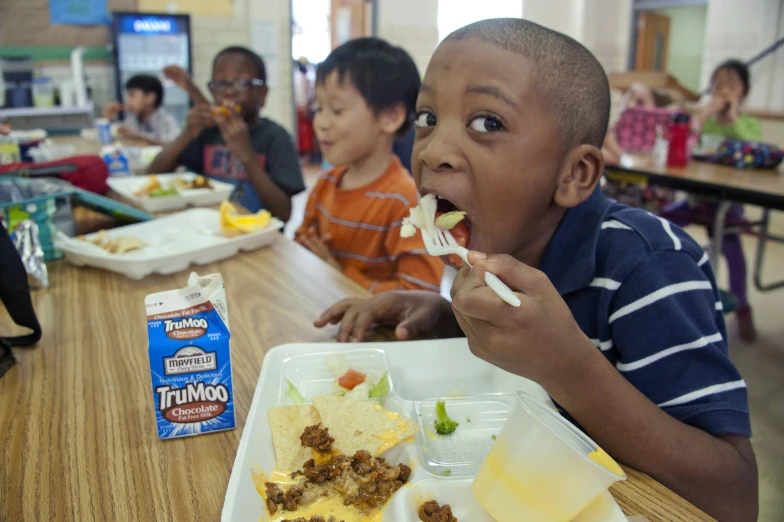 the young child is eating his lunch while others watch