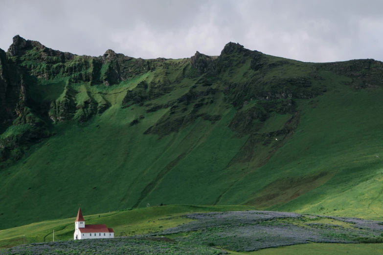 a hill with a white church and a green pasture on the hillside