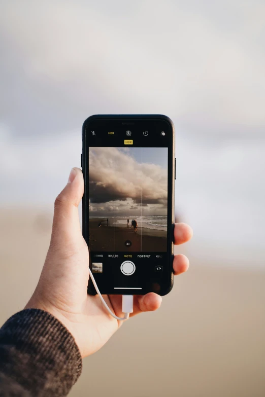 the person holds up a cell phone that displays the scene of two people walking down a beach
