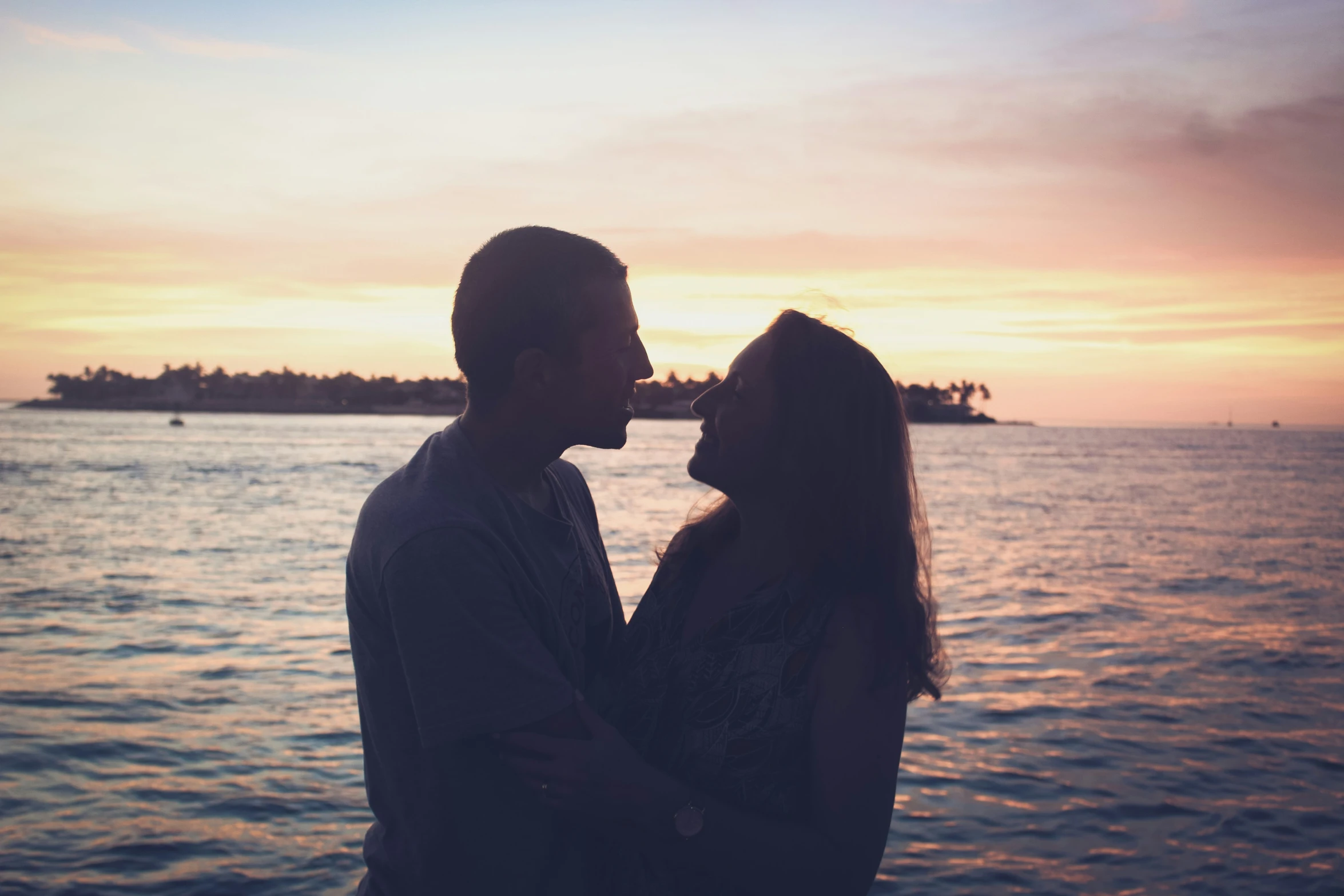 a couple emce while looking at the water with a bright sunset