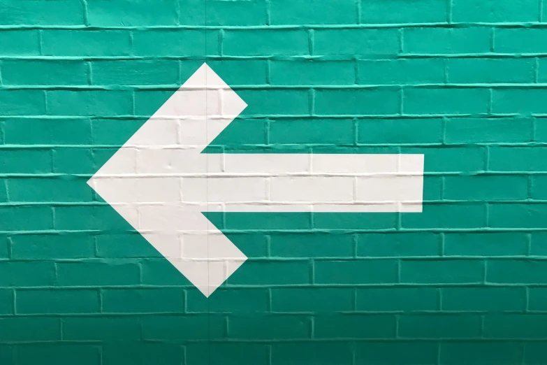 the arrow is pointing sideways against a green brick wall