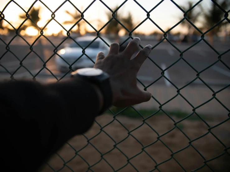 a man standing behind a fence, reaching for soing