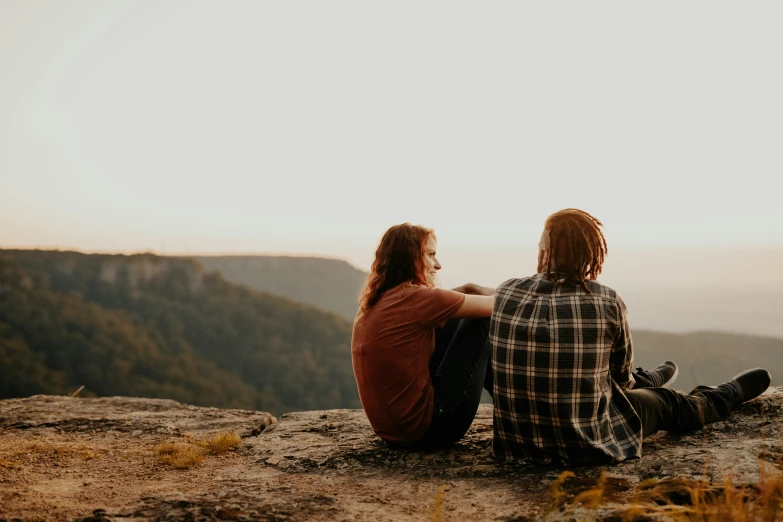 a man and woman sitting on the top of a hill