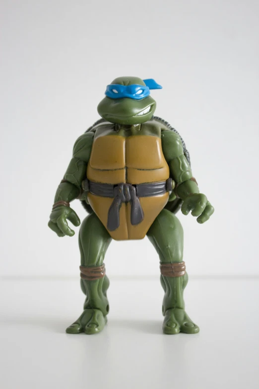 a toy turtle is wearing blue mask and holding a green object