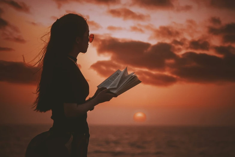 a person reading a book at sunset on a beach