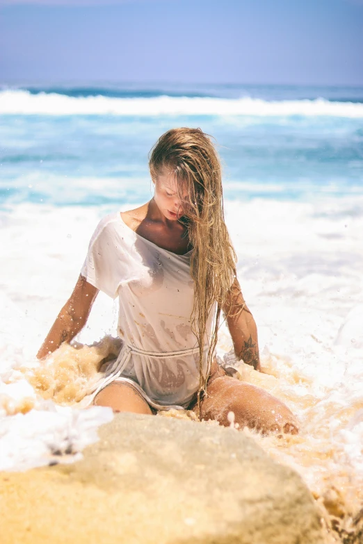 a woman sitting on a beach while holding a long brown pony tail