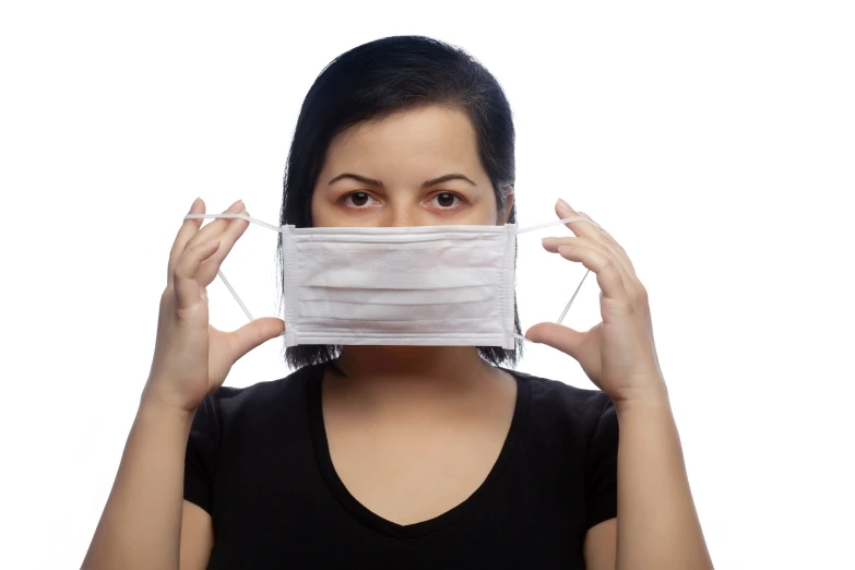 a woman wearing a white mask holds a piece of cloth to her face