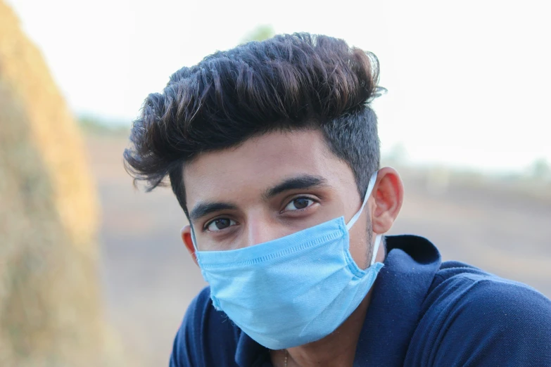 a young man with a messy up top and wearing a face mask