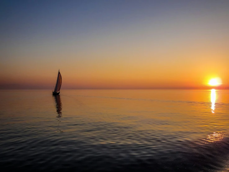 the sun sets as a sailboat is in the ocean