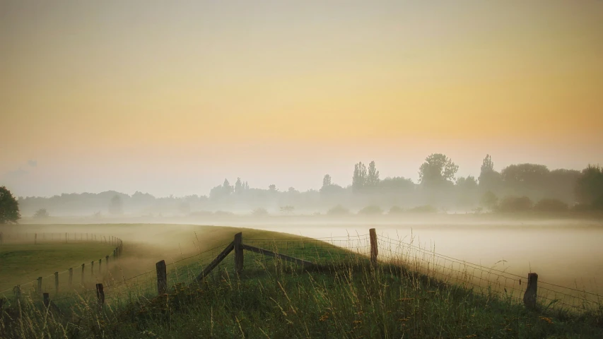 a rural area is in the foreground with a lake in the middle and fog hanging over it