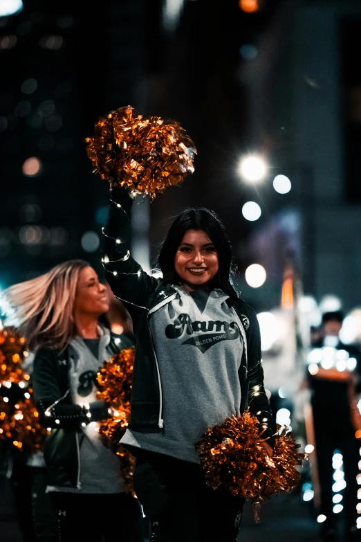 a girl with a black and white uniform is smiling while holding two orange and silver pom - poms