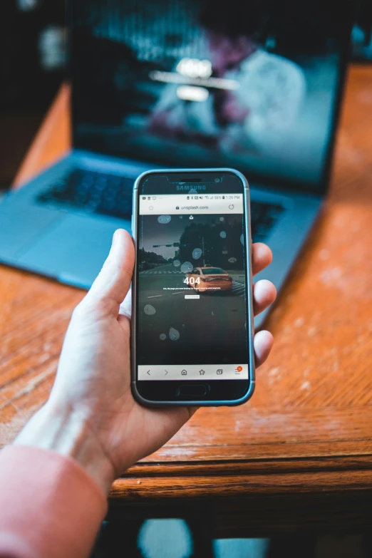 a person holding a smart phone while sitting at a desk with a laptop