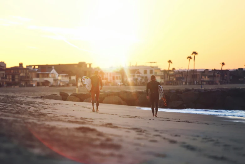 two men are walking towards the ocean at sunset