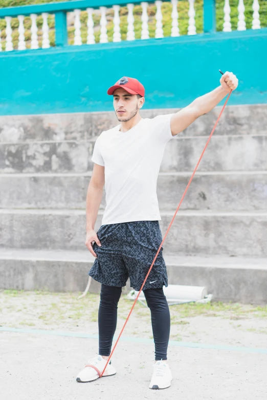 a man wearing all black stands with his hand on one side and holds onto a rope in one hand