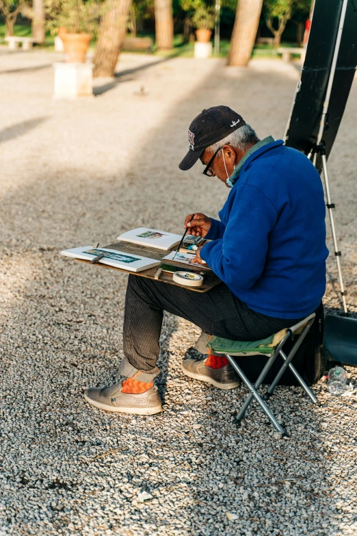 an old man sitting at a picnic table painting